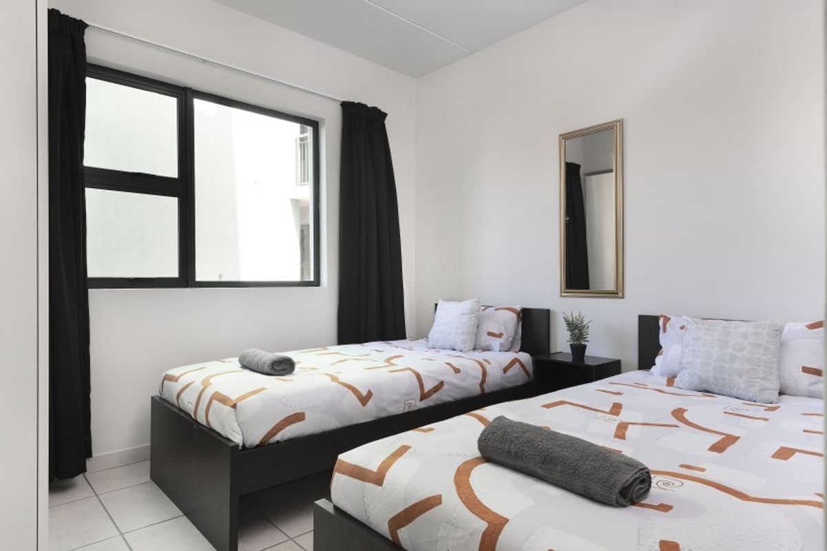 A bright bedroom featuring tiled flooring and a large window with black frames, providing natural light.