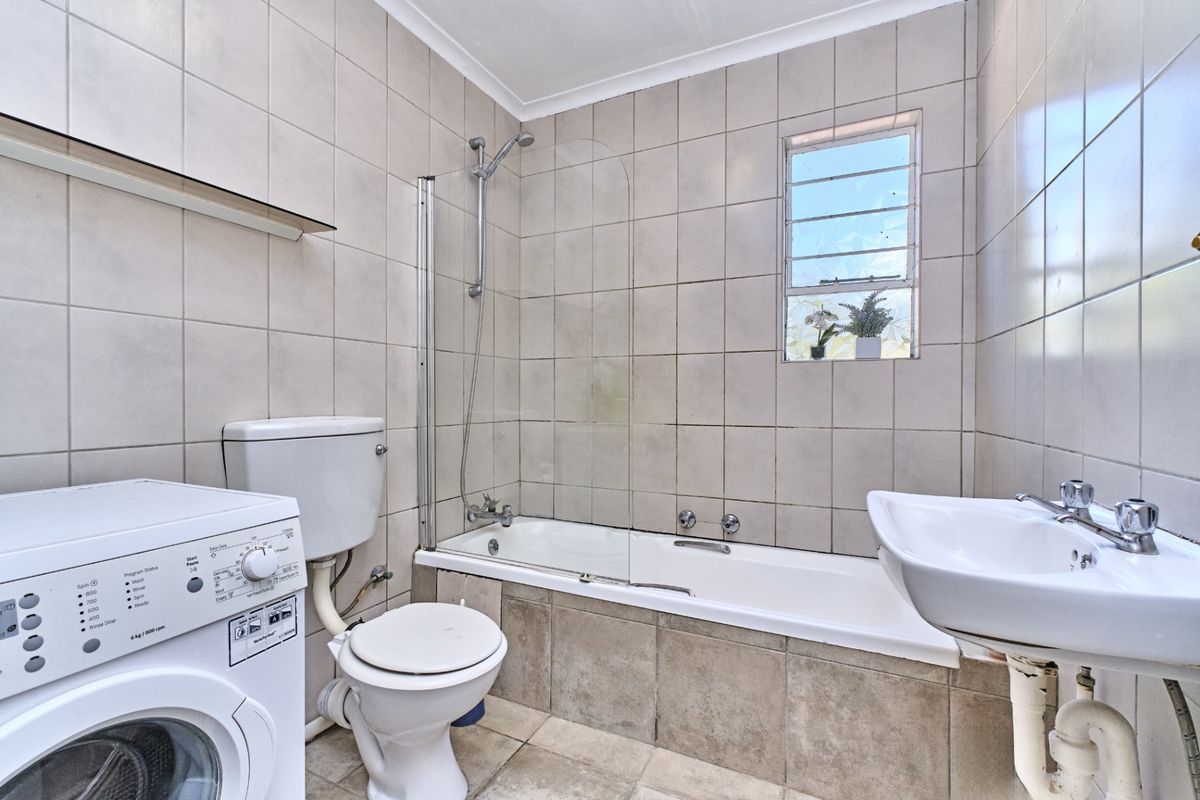 A functional bathroom featuring a bathtub with a glass shower screen, a pedestal basin, a toilet, and a dedicated space for a washing machine.
