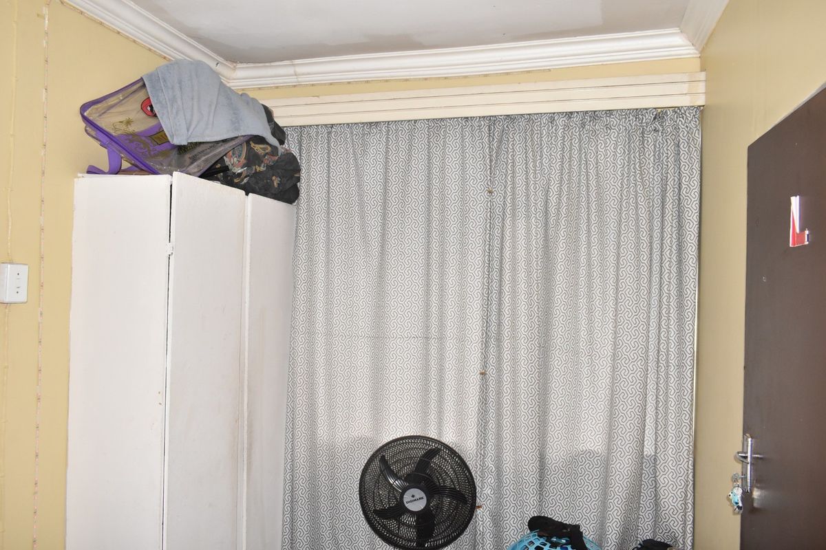 A bedroom interior featuring crown molding and a curtain track, showing signs of wear on the ceiling and wall finishes.