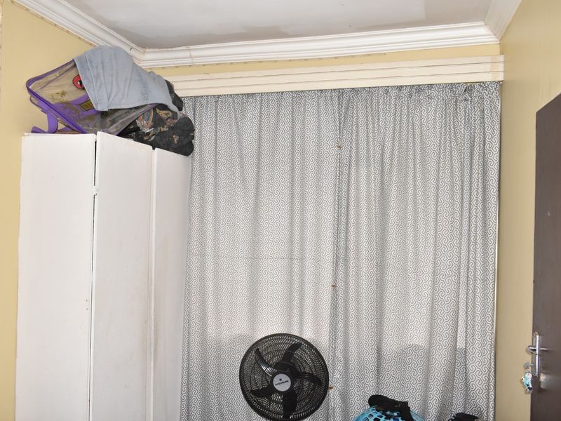 A bedroom interior featuring crown molding and a curtain track, showing signs of wear on the ceiling and wall finishes.
