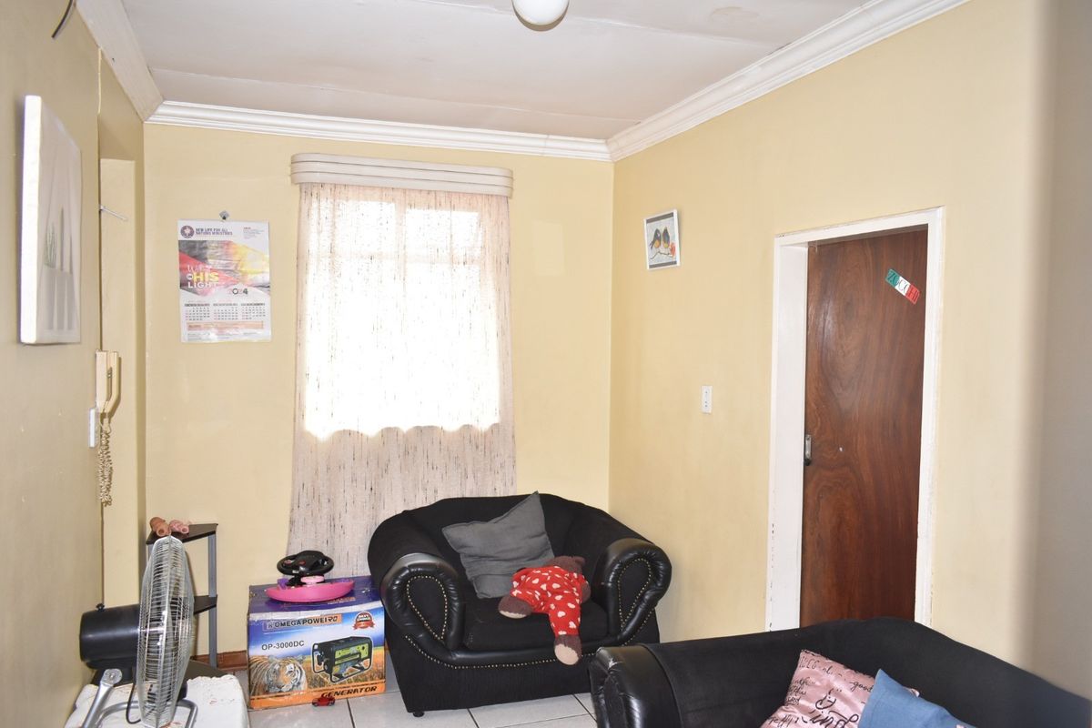 A living room featuring tiled flooring and decorative cornicing, currently showing signs of wear on the ceiling and walls.