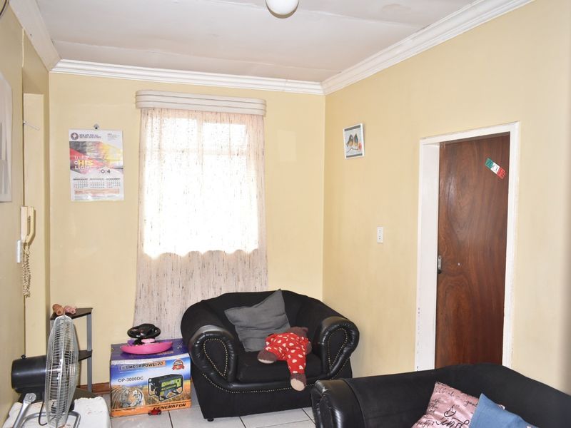 A living room featuring tiled flooring and decorative cornicing, currently showing signs of wear on the ceiling and walls.