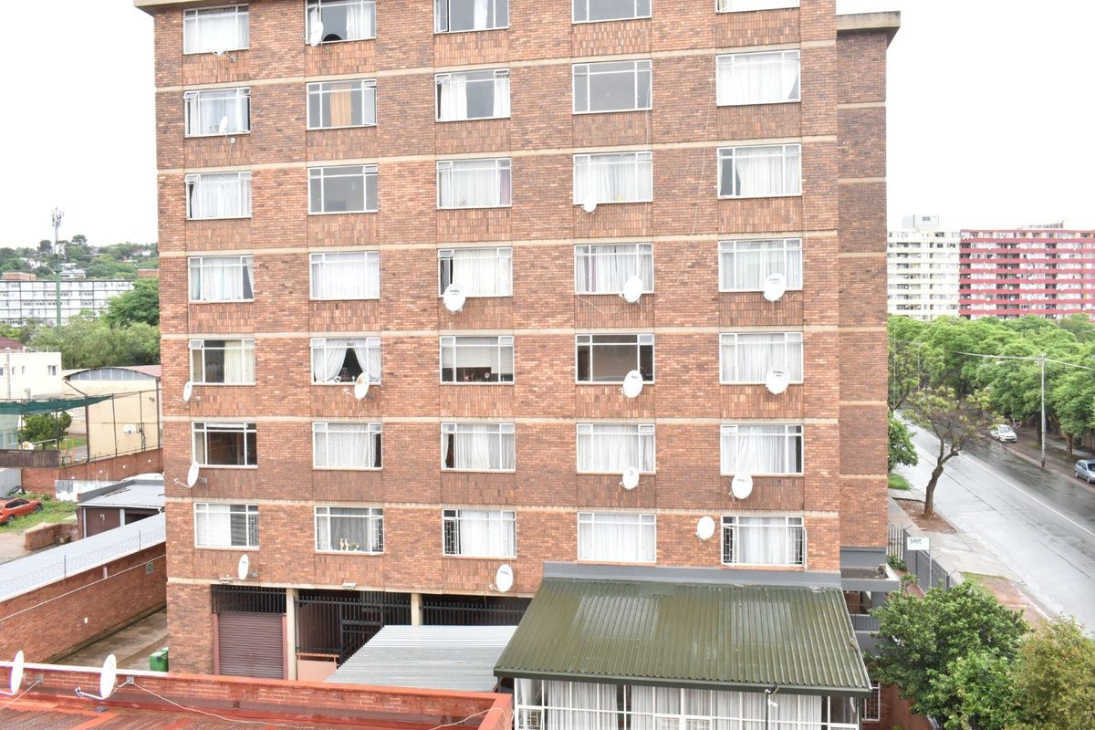 Exterior view of a multi-story brick apartment building featuring multiple windows and installed satellite dishes.