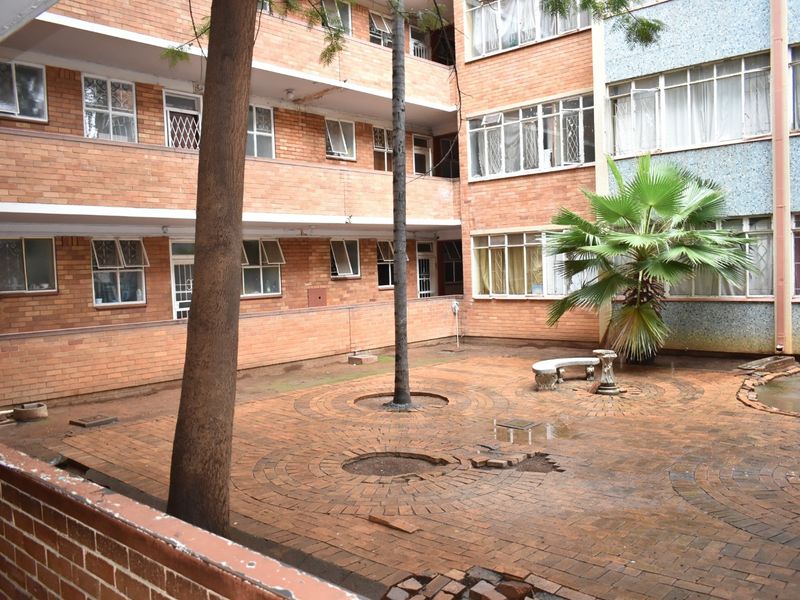 A communal courtyard area featuring brick paving and multi-story brick apartment facades with security-fitted windows.