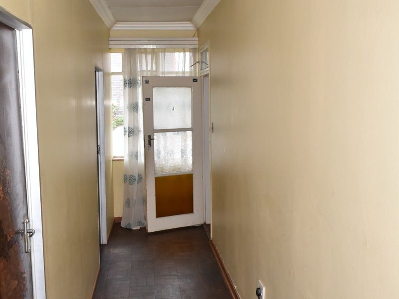 A functional hallway featuring parquet flooring, coved ceilings, and a timber door leading to an exterior space.