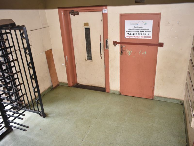 A utilitarian apartment building entrance area featuring a security gate, service doors, and wall-mounted mailboxes with visible wear on finishes.