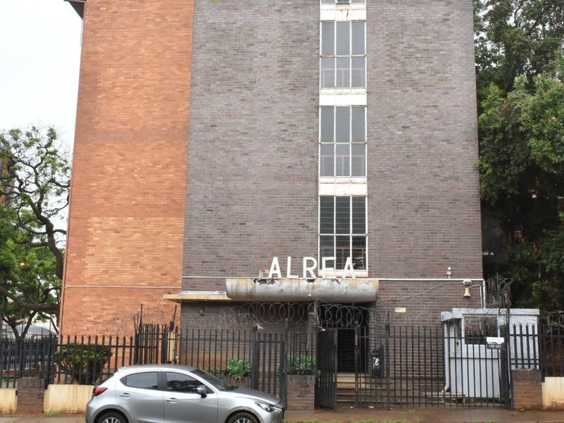 Front elevation of the Alrea apartment building featuring a brick facade, secure gated entrance, and a dedicated security guard booth.