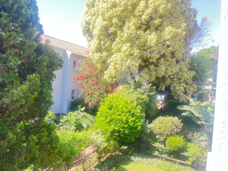 A view overlooking a lush, well-maintained garden with mature trees and greenery, providing a peaceful outlook from the apartment.