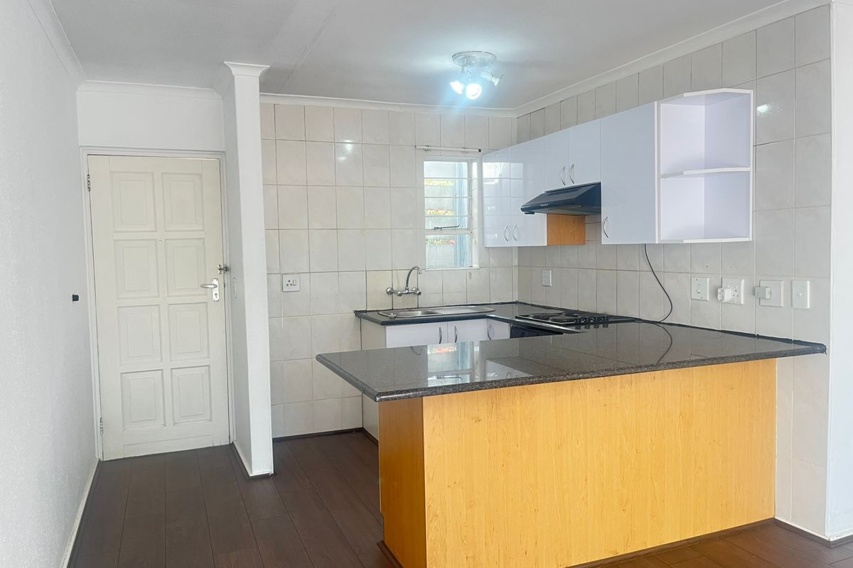 A clean, functional kitchen featuring granite countertops, built-in cabinetry, a hob with extractor fan, and a double sink with tiled backsplash.