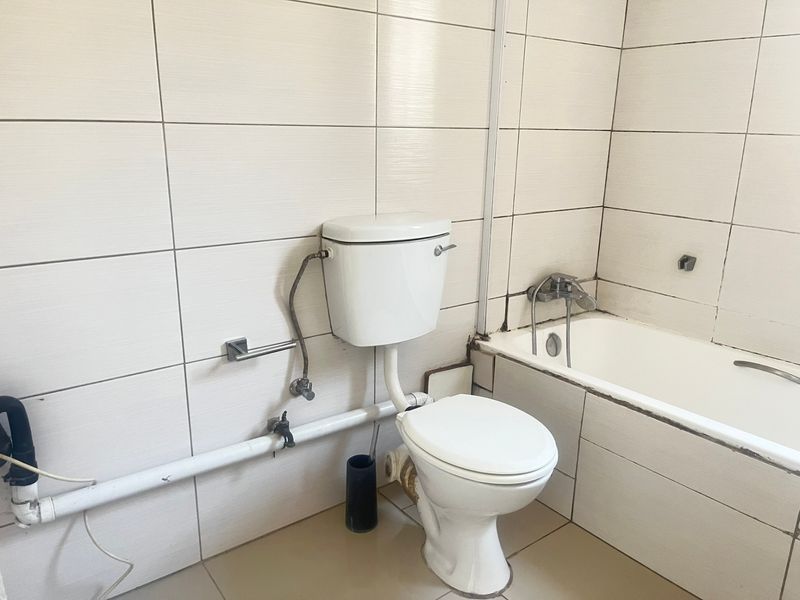 A functional bathroom featuring tiled walls and floors, a standard toilet, and a bathtub with exposed plumbing fixtures.