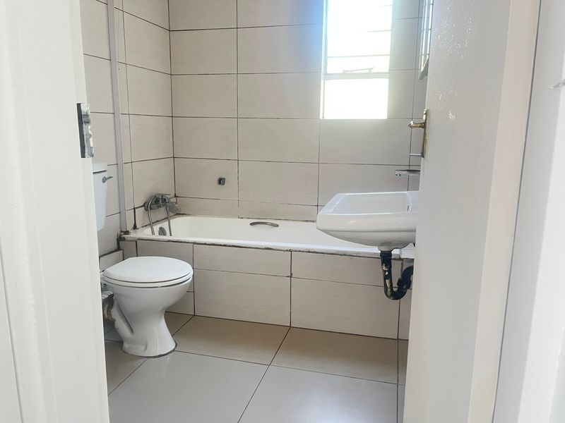 A functional bathroom featuring a bathtub, toilet, and wall-mounted basin with neutral ceramic tiling throughout.