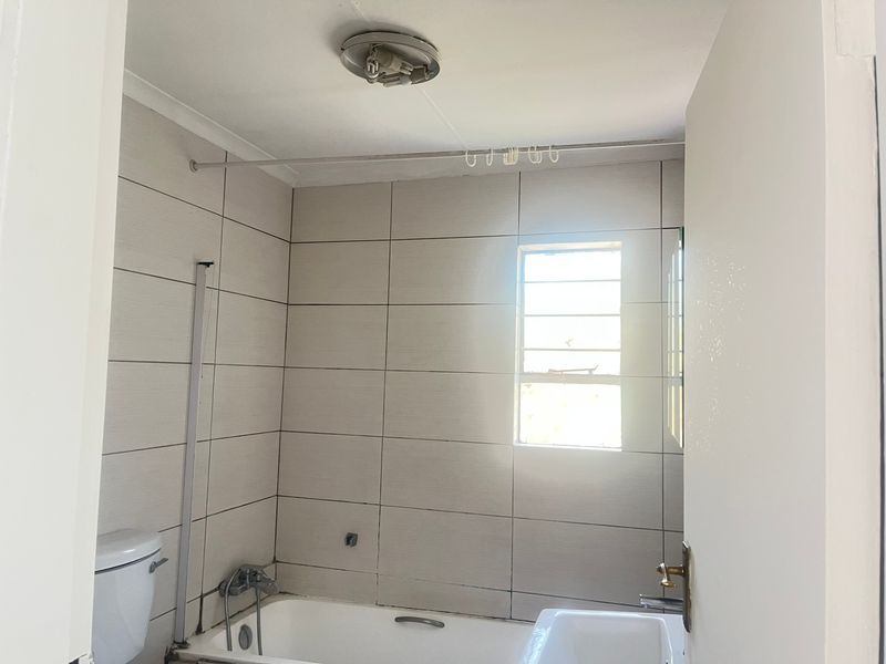 A functional bathroom featuring tiled walls, a bathtub, and a toilet, requiring minor maintenance and cosmetic updates to improve its overall condition.
