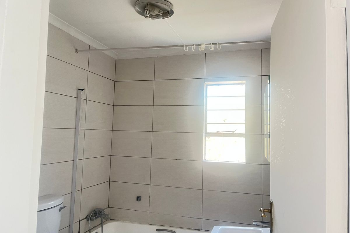 A functional bathroom featuring tiled walls, a bathtub, and a toilet, requiring minor maintenance and cosmetic updates to improve its overall condition.
