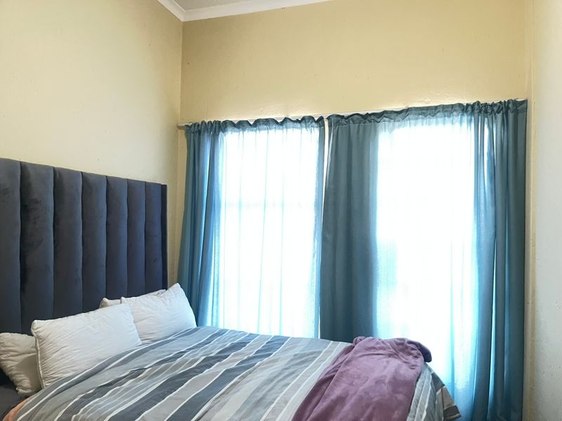 A bedroom featuring a neutral wall finish and a window dressed with blue curtains.