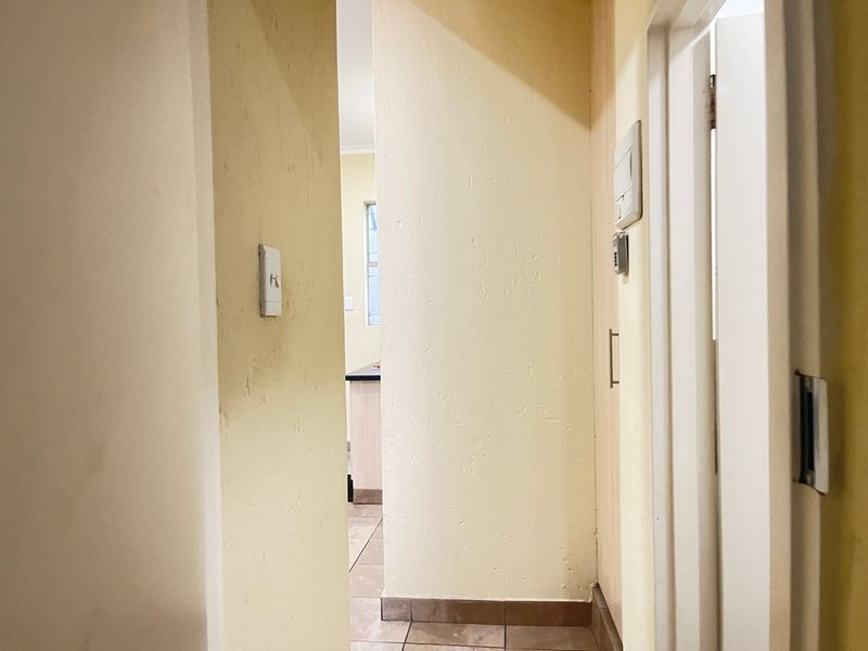 A narrow hallway with tiled flooring and an intercom system, leading towards an adjacent room.