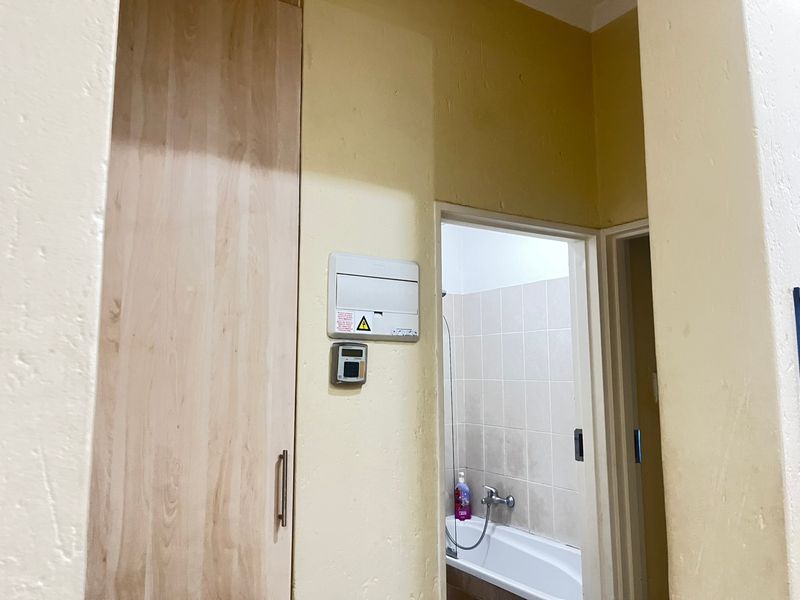 A hallway area featuring a built-in cupboard, electrical distribution board, and alarm keypad, with a view into an adjacent bathroom.