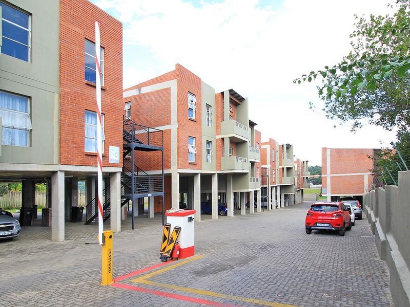 Exterior view of a multi-story apartment complex featuring brick facades, concrete support pillars, and a secure gated entrance with paved driveway access.