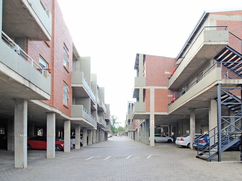 Exterior view of a multi-story apartment complex featuring exposed brick facades, concrete support pillars, and covered parking areas with external staircases.