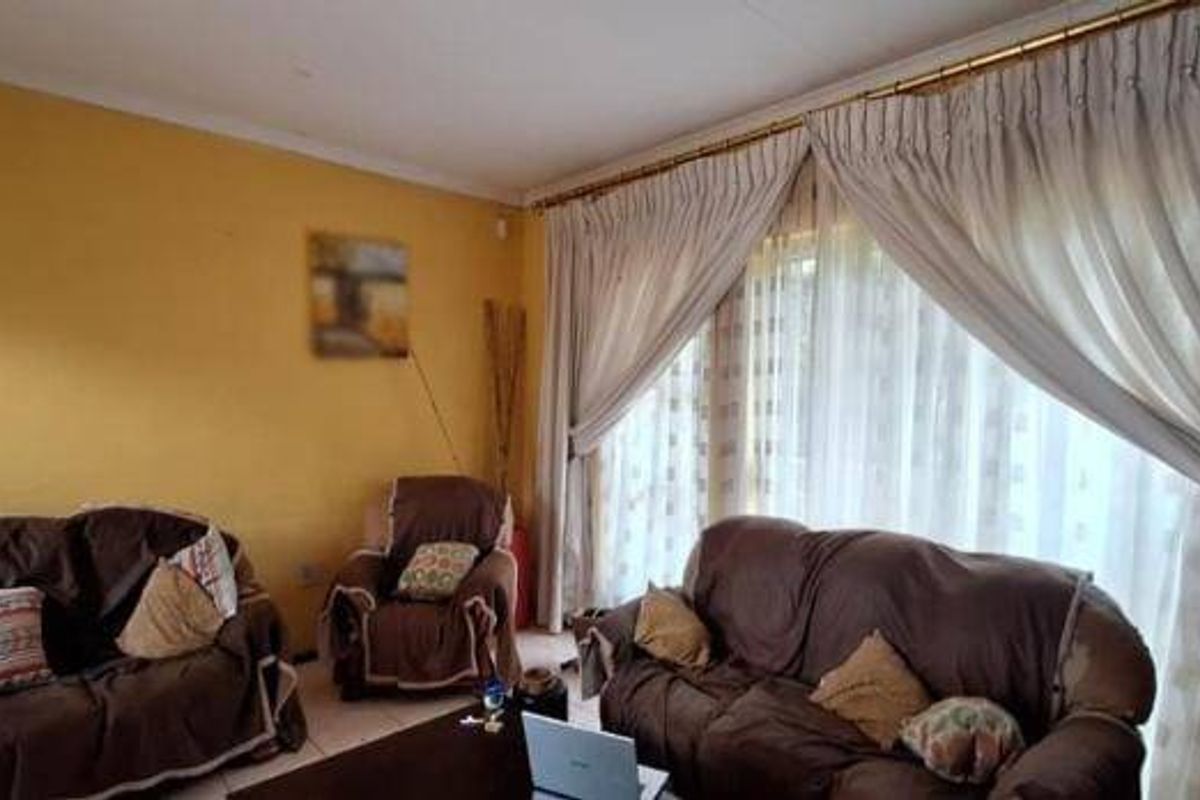 A living room featuring tiled flooring and large windows dressed with floor-to-ceiling curtains.