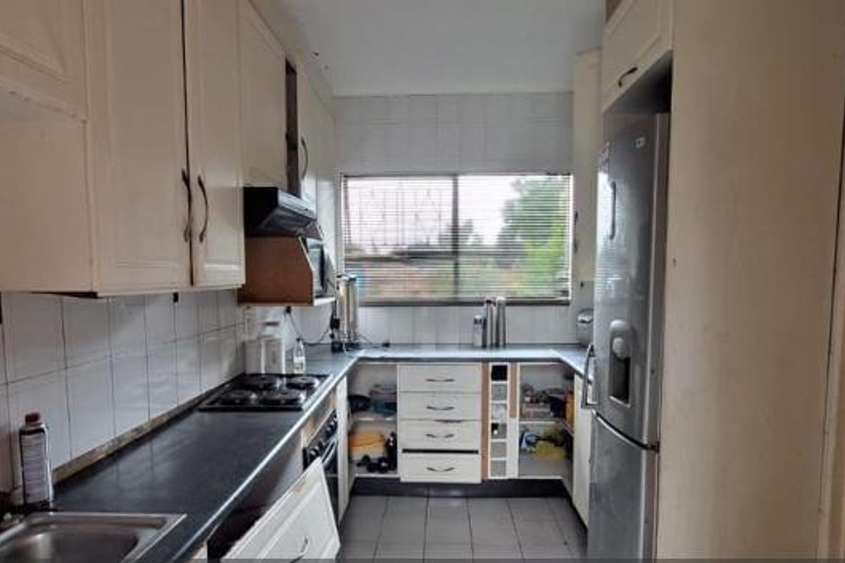 A functional kitchen featuring built-in cabinetry, a gas hob with extractor, and tiled splashbacks. The space would benefit from cosmetic updates to modernize finishes.