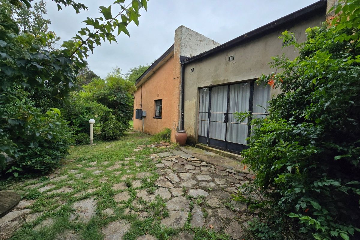 Rear exterior view of the property featuring a stone-paved patio area, sliding glass doors, and established garden surroundings.