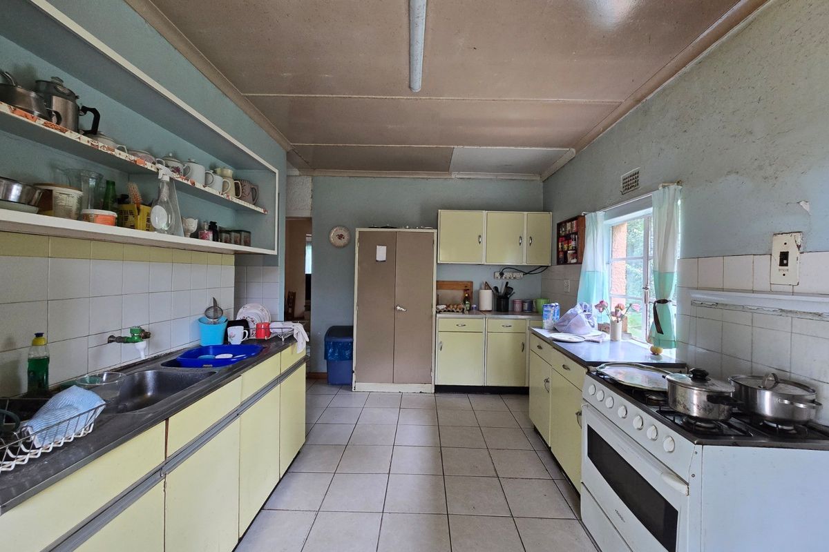 A dated kitchen featuring original cabinetry, tiled flooring, and a double sink, requiring cosmetic updates to modernize the space.