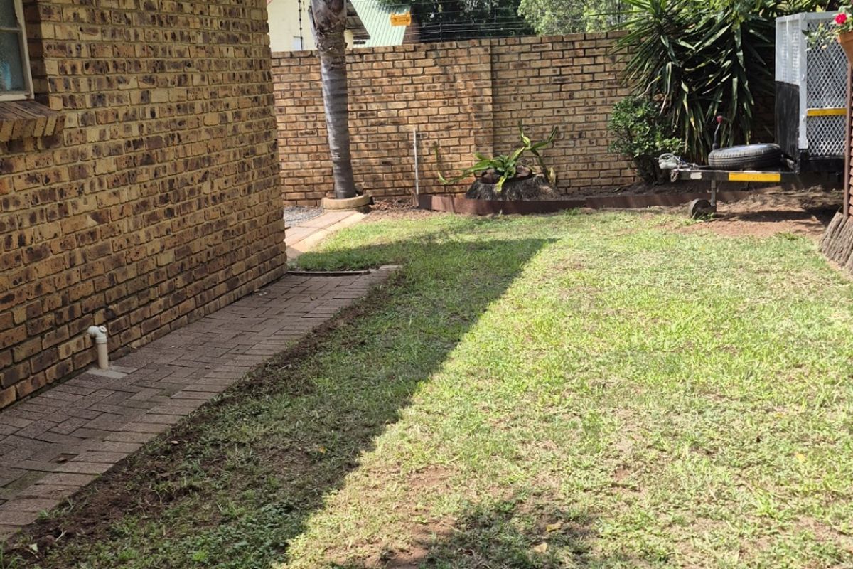 A private rear garden area featuring a face brick townhouse exterior, a paved walkway, and a perimeter boundary wall.