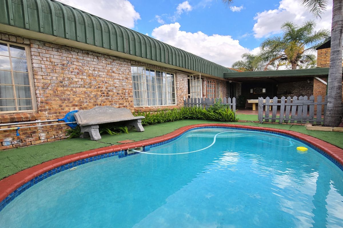 Outdoor pool area featuring a swimming pool, brick facade, and a covered patio space with artificial grass surfacing.