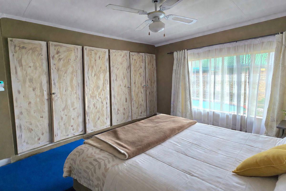 A bedroom featuring built-in cupboards, a ceiling fan, and large windows allowing natural light.