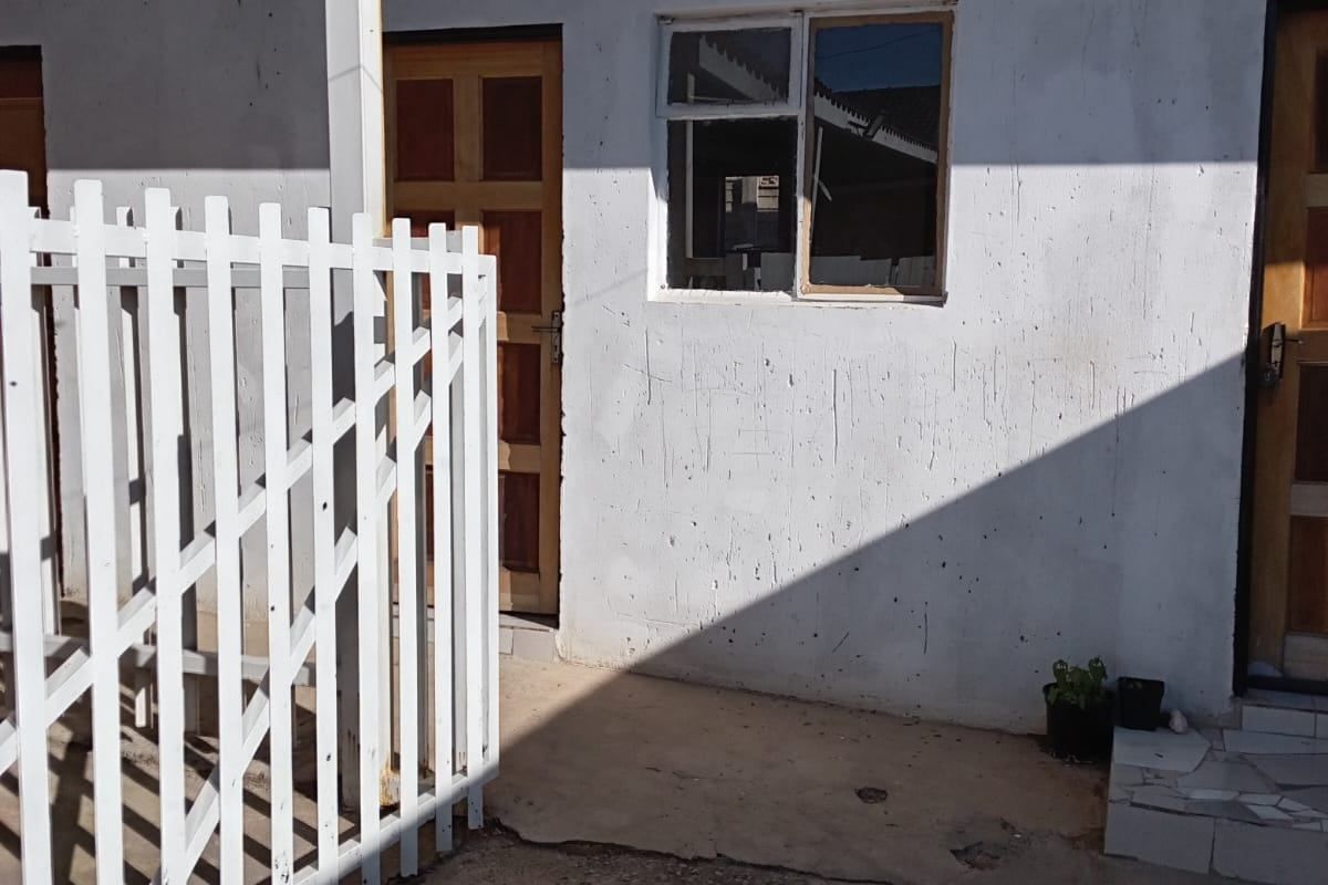 Exterior view of an apartment entrance featuring a small covered patio area, concrete paving, and wooden doors with a white picket fence.