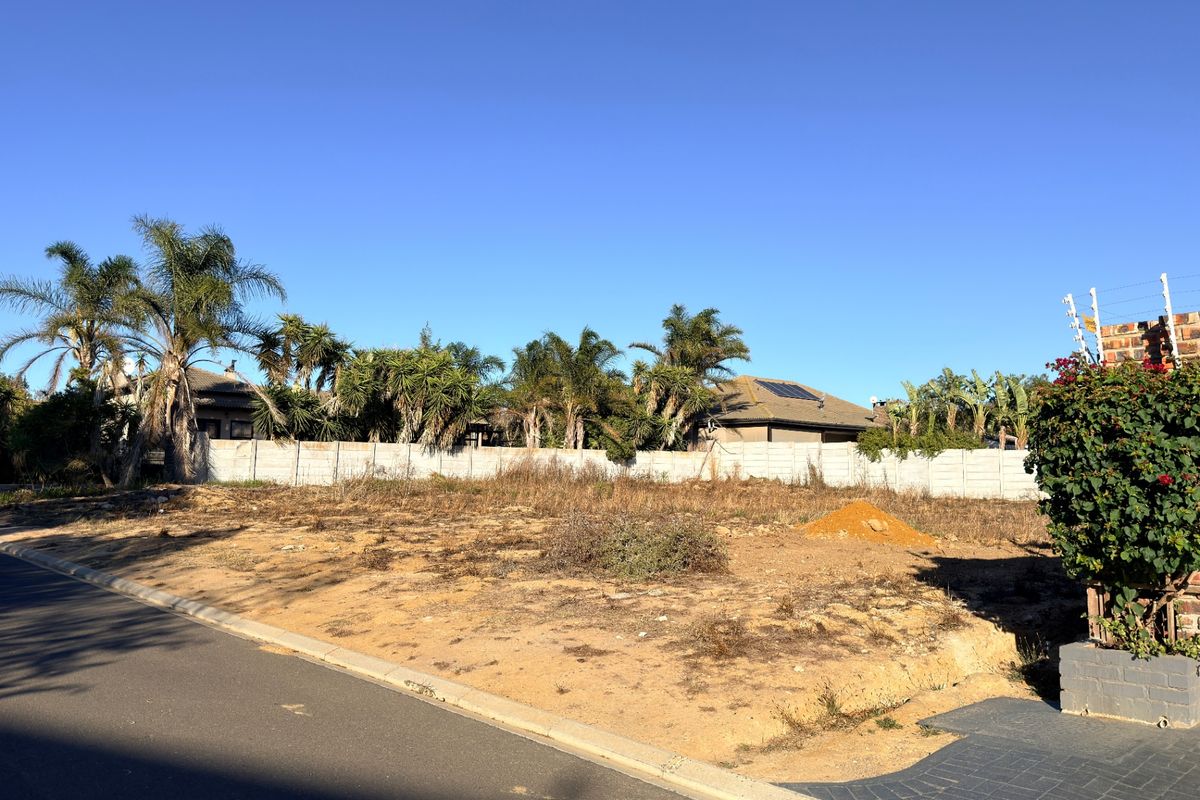 A vacant residential plot featuring a concrete boundary wall with electric fencing, situated in a developed neighborhood.