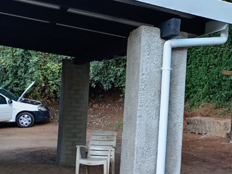 A simple open-sided carport structure featuring concrete support pillars and a metal roof, situated in a natural outdoor setting.