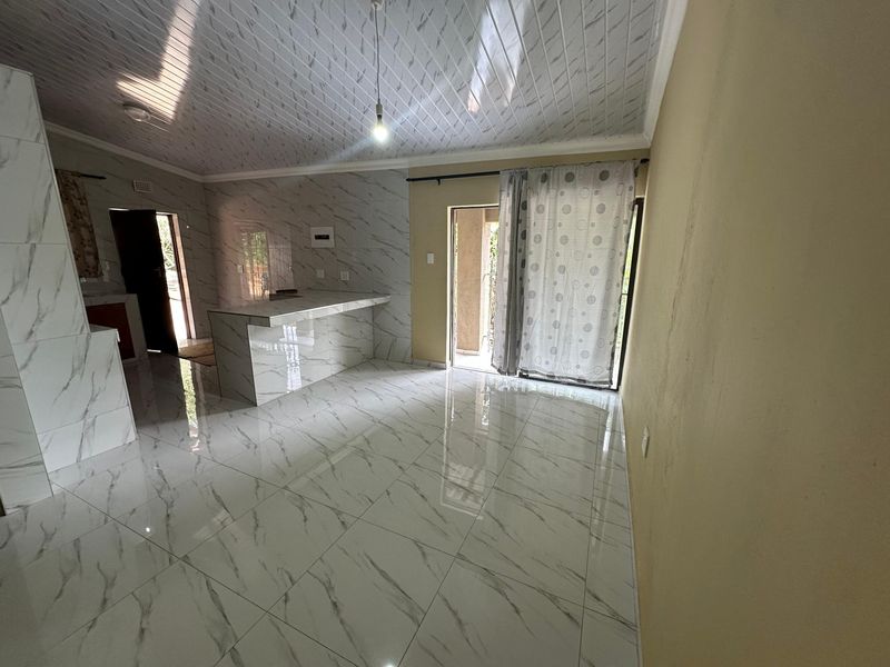 Open-plan living and kitchen area featuring marble-look floor tiles, a matching kitchen island, and a sliding glass door leading to the exterior.
