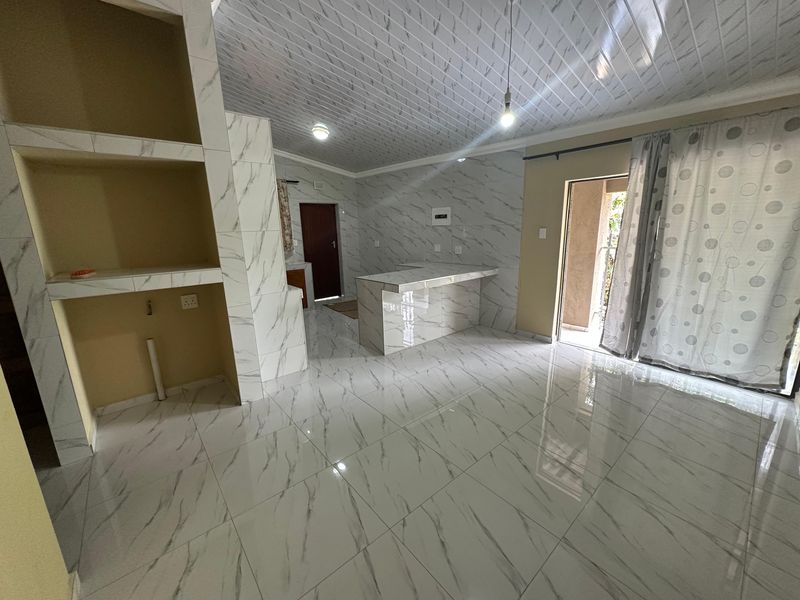 An open-plan living and kitchen area featuring marble-look tiled floors, a matching kitchen island, and a sliding door leading to an outdoor space.