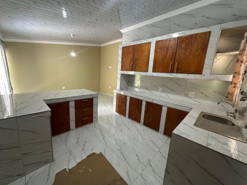 A modern kitchen featuring marble-effect tiling on floors and counters, paired with wooden cabinetry. The space is currently unfinished and awaiting final touches.