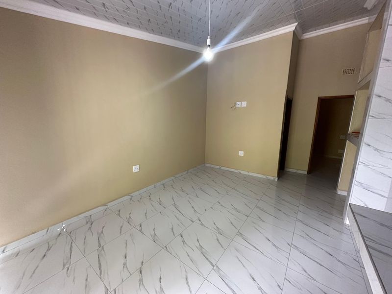 An empty open-plan living area featuring modern marble-look floor tiles, neutral wall paint, and a textured ceiling with a central pendant light fitting.