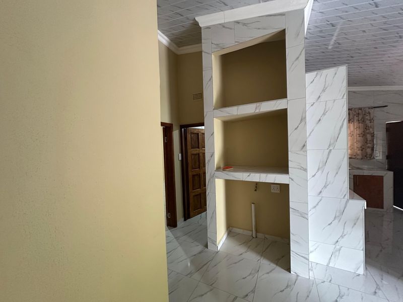 An open-plan living area featuring modern marble-effect floor tiles and a central tiled partition wall with built-in shelving and utility connections.