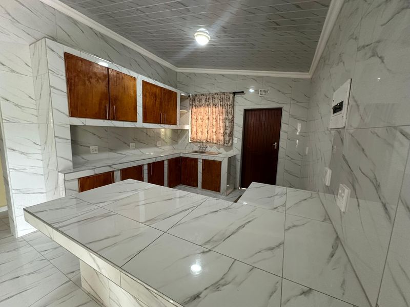 A spacious kitchen featuring extensive marble-look wall tiling, built-in wooden cabinetry, and a large breakfast bar, offering a clean and functional layout.