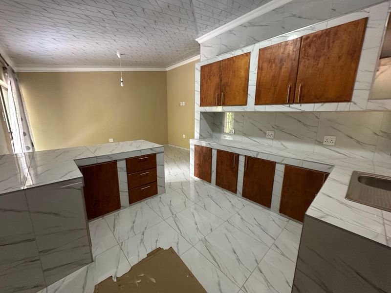A modern kitchen featuring marble-effect tiled surfaces, wooden cabinetry, and a central island, currently awaiting final finishing touches.