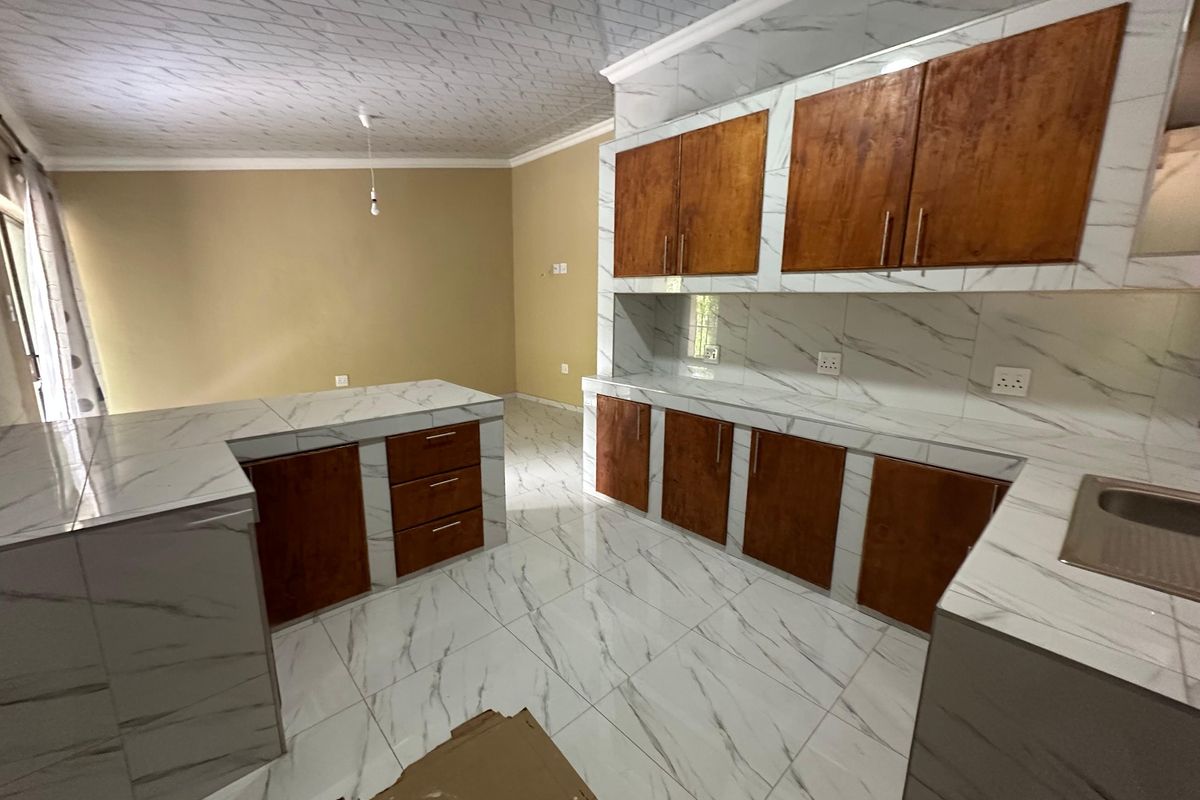 A modern kitchen featuring marble-effect tiled surfaces, wooden cabinetry, and a central island, currently awaiting final finishing touches.