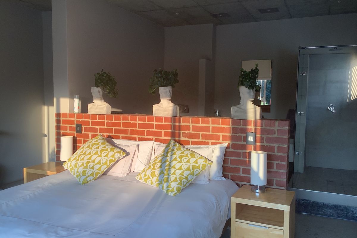 A modern bedroom featuring an exposed brick partition wall, concrete ceiling, and an en-suite shower area with glass enclosure.