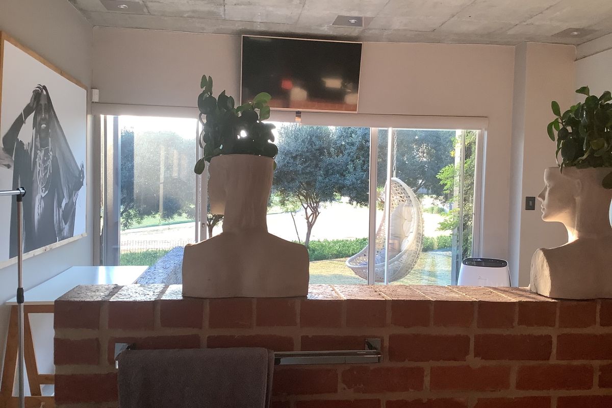 A living area featuring a raw concrete ceiling, exposed brick partition wall, and large sliding glass doors providing views of the garden.