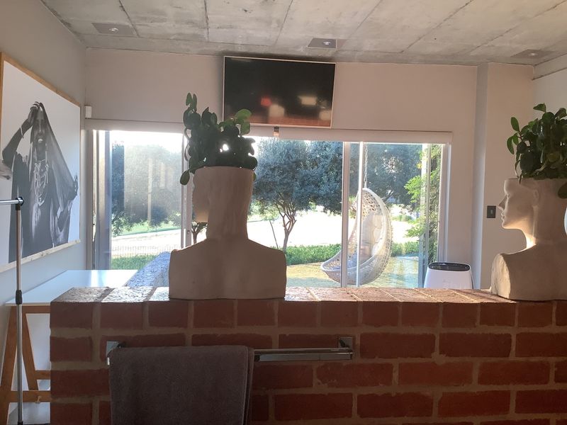 A living area featuring a raw concrete ceiling, exposed brick partition wall, and large sliding glass doors providing views of the garden.