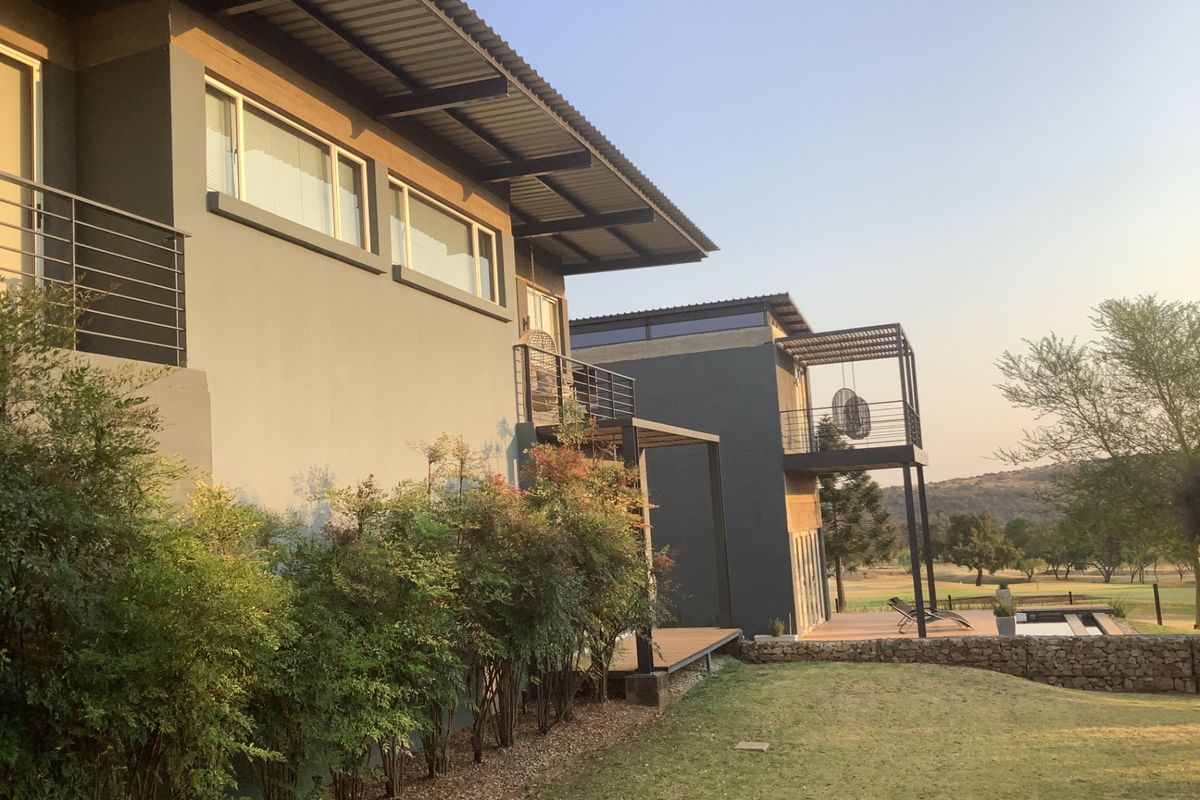 Rear view of a modern multi-level home featuring balconies, metal roofing, and a landscaped garden overlooking a golf course.