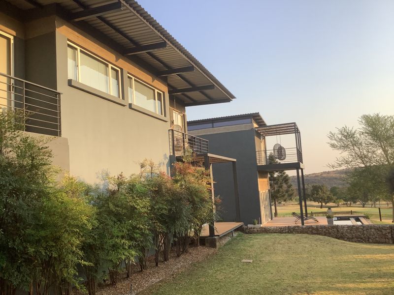 Rear view of a modern multi-level home featuring balconies, metal roofing, and a landscaped garden overlooking a golf course.
