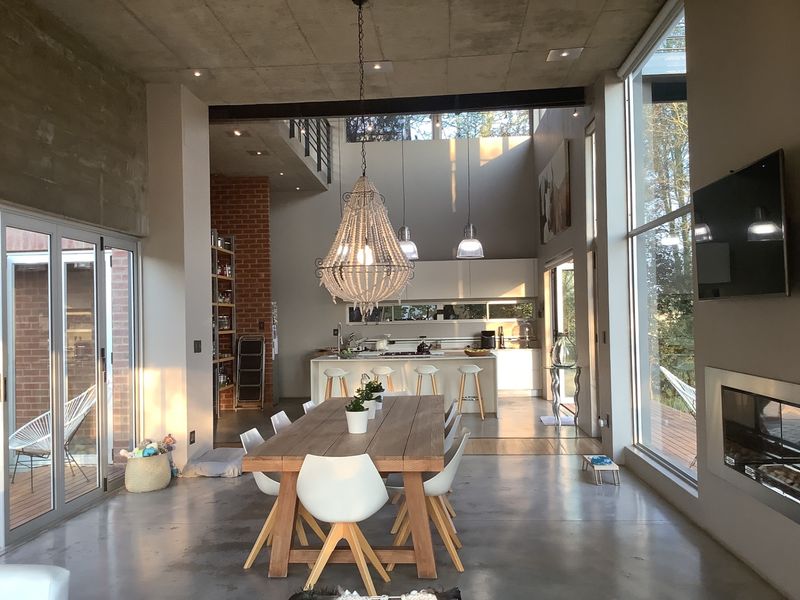 Spacious open-plan living and dining area featuring polished concrete floors, high ceilings, a modern kitchen with island, and large glass sliding doors.