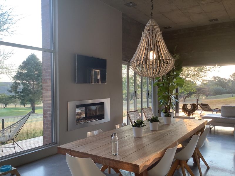 Modern open-plan dining area featuring a built-in fireplace, polished concrete ceilings, and floor-to-ceiling glass doors opening onto a scenic outdoor deck.