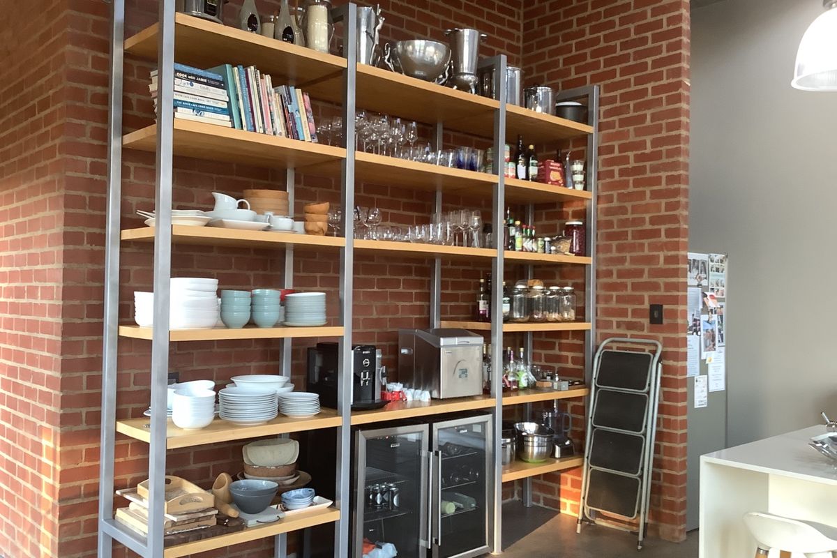 A kitchen area featuring exposed brick walls, industrial-style metal shelving units, and a built-in under-counter beverage fridge.