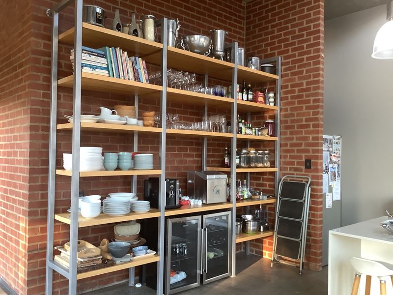 A kitchen area featuring exposed brick walls, industrial-style metal shelving units, and a built-in under-counter beverage fridge.
