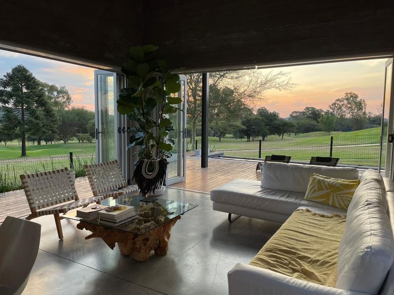 Modern open-plan living area featuring polished concrete floors and expansive bi-fold doors opening onto a wooden deck with scenic golf course views.